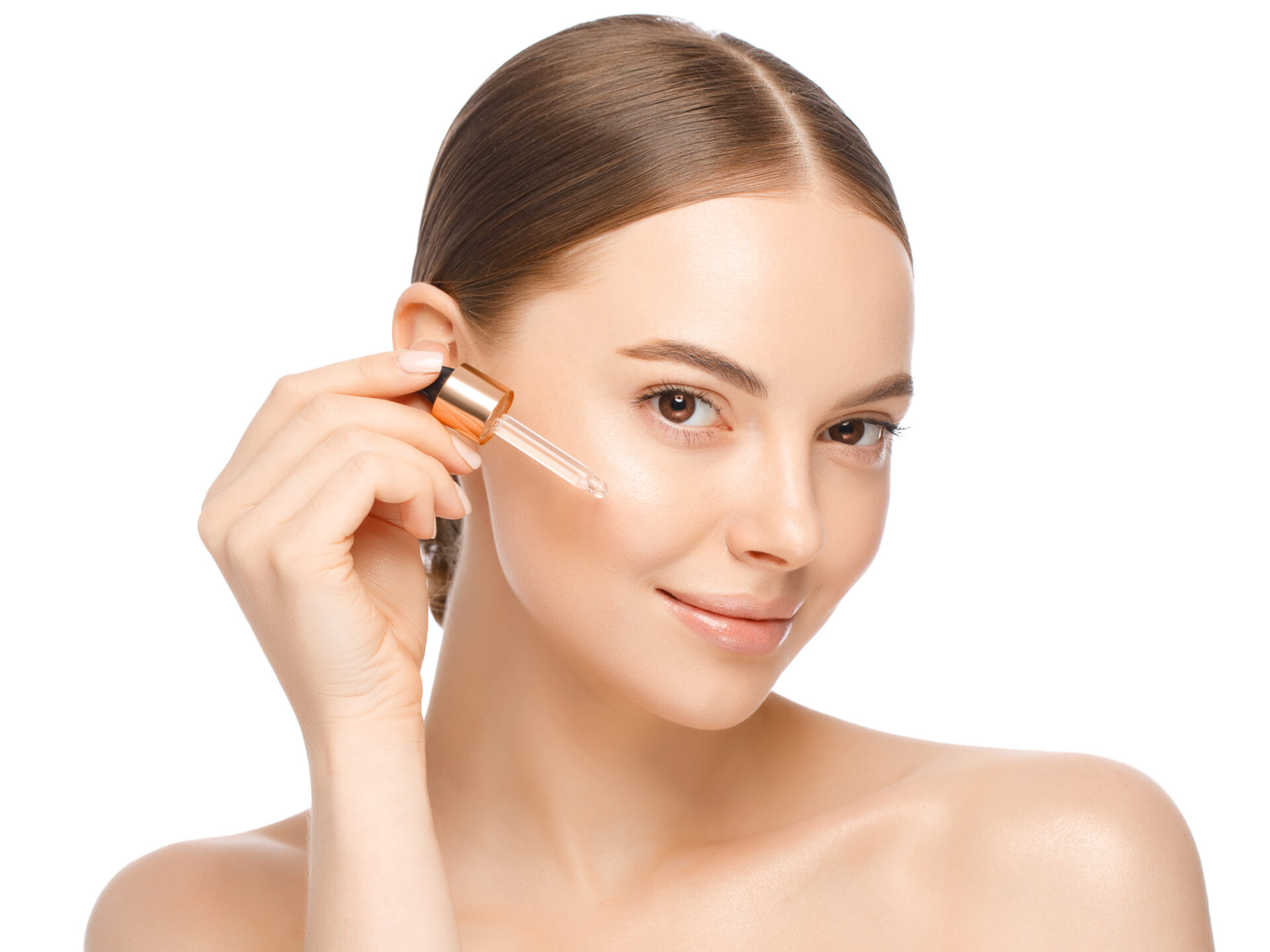 Young woman applying serum to her face, looking at camera, isolated on white background. Beautiful model with perfect clean fresh skin. Treatment or cosmetic ads